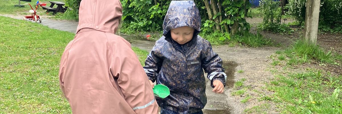 Børn i regnvejr på legepladsen i Børnehuset Mælkevejen