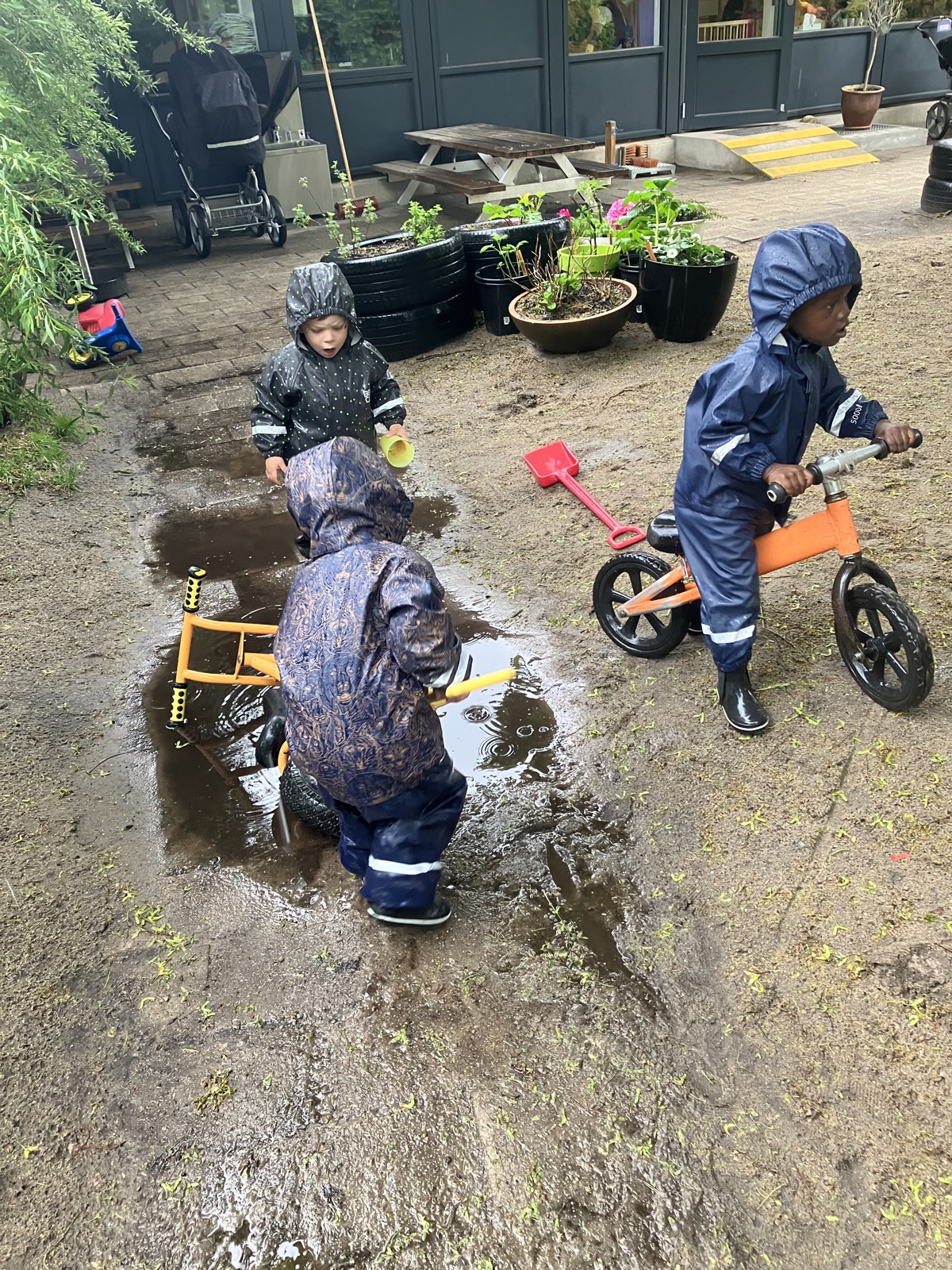 Børn i regnvejr på legepladsen i Børnehuset Mælkevejen