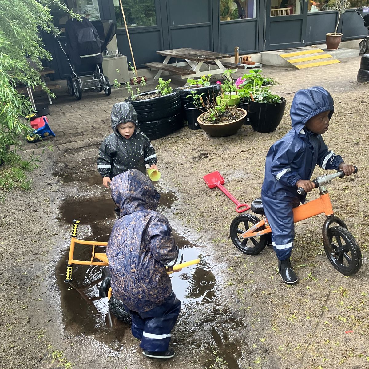 Børn i regnvejr på legepladsen i Børnehuset Mælkevejen