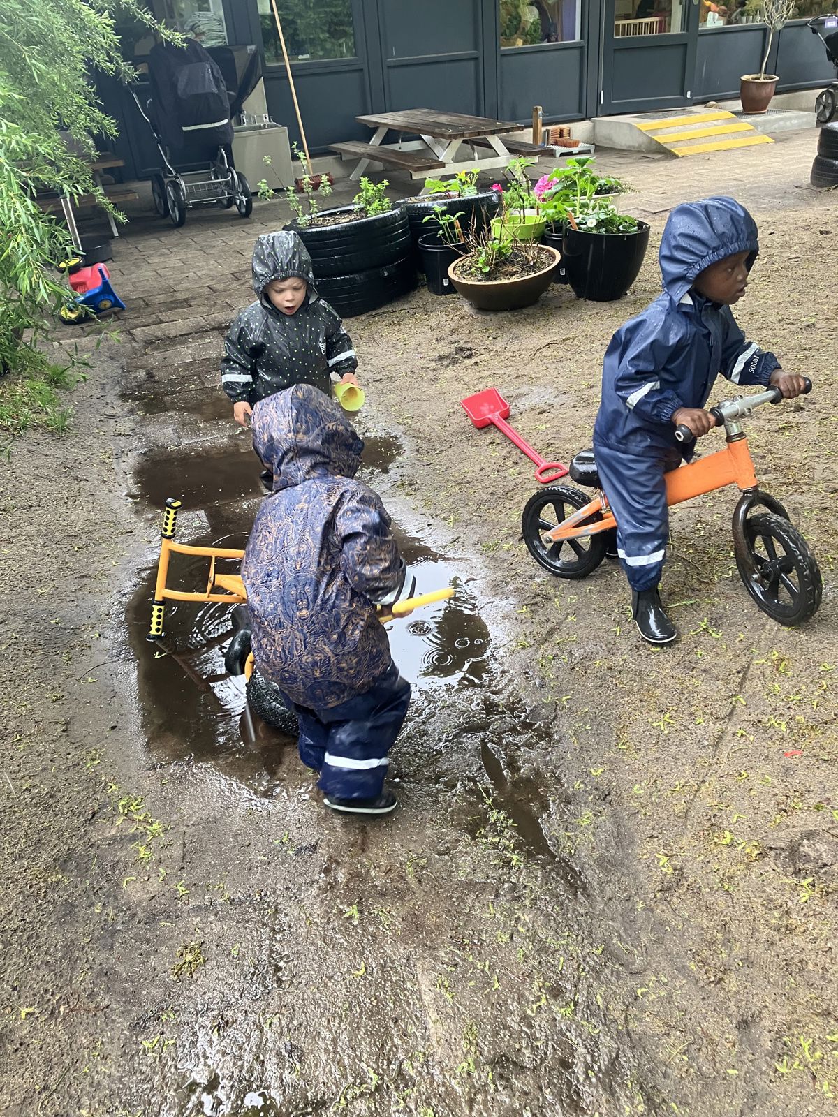 Børn i regnvejr på legepladsen i Børnehuset Mælkevejen