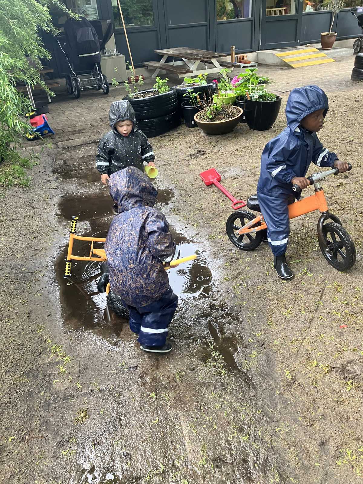 Børn i regnvejr på legepladsen i Børnehuset Mælkevejen